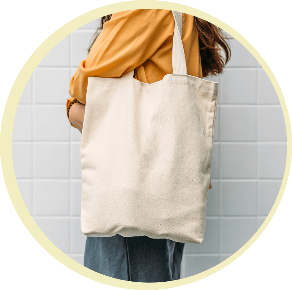 Person holding a beige canvas tote bag against a tiled wall.