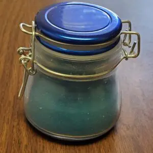 Small glass jar with blue lid containing a blue-green substance.