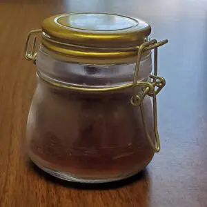 A small glass jar with a yellow lid on a wooden surface.