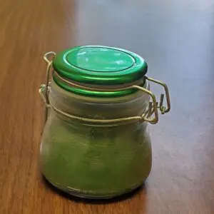 A small glass jar with a green lid containing green powder.