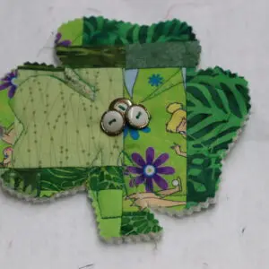 Handmade fabric frog with button eyes on a leafy background.