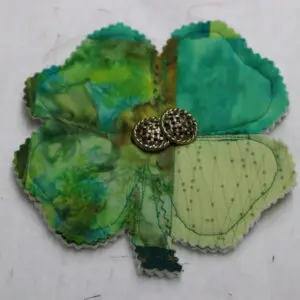 Handmade fabric flower brooch with green and blue petals and a beaded center.