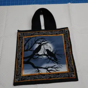 Black tote bag with a witch and raven design under a full moon.