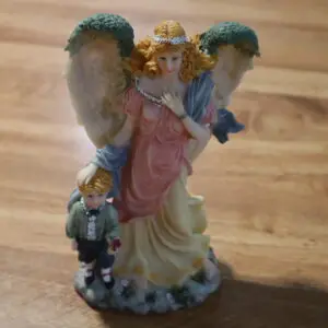 Porcelain angel figurine with two children on a wooden floor.