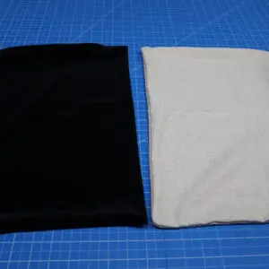 Two folded pieces of fabric, one black and one white, on a blue cutting mat.