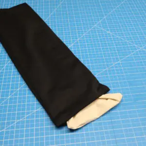 Black fabric sleeve with a beige lining on a blue cutting mat.