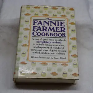 The Fannie Farmer Cookbook, a classic cooking guide with a worn cover.