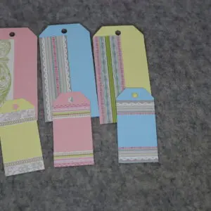 Three colorful paper bookmarks with delicate designs on a gray surface.