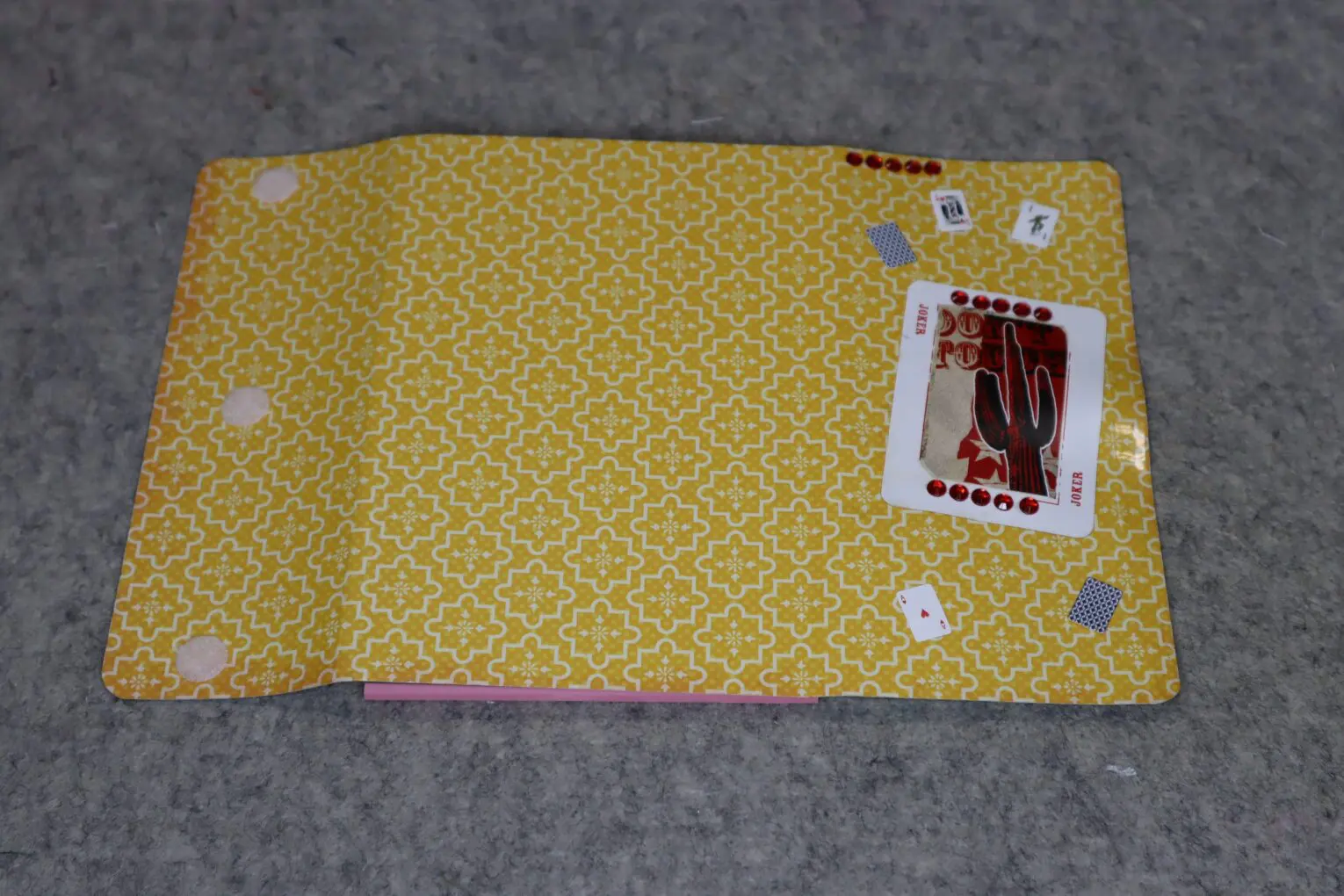 A yellow patterned wallet with playing cards and a stamp on a gray surface.