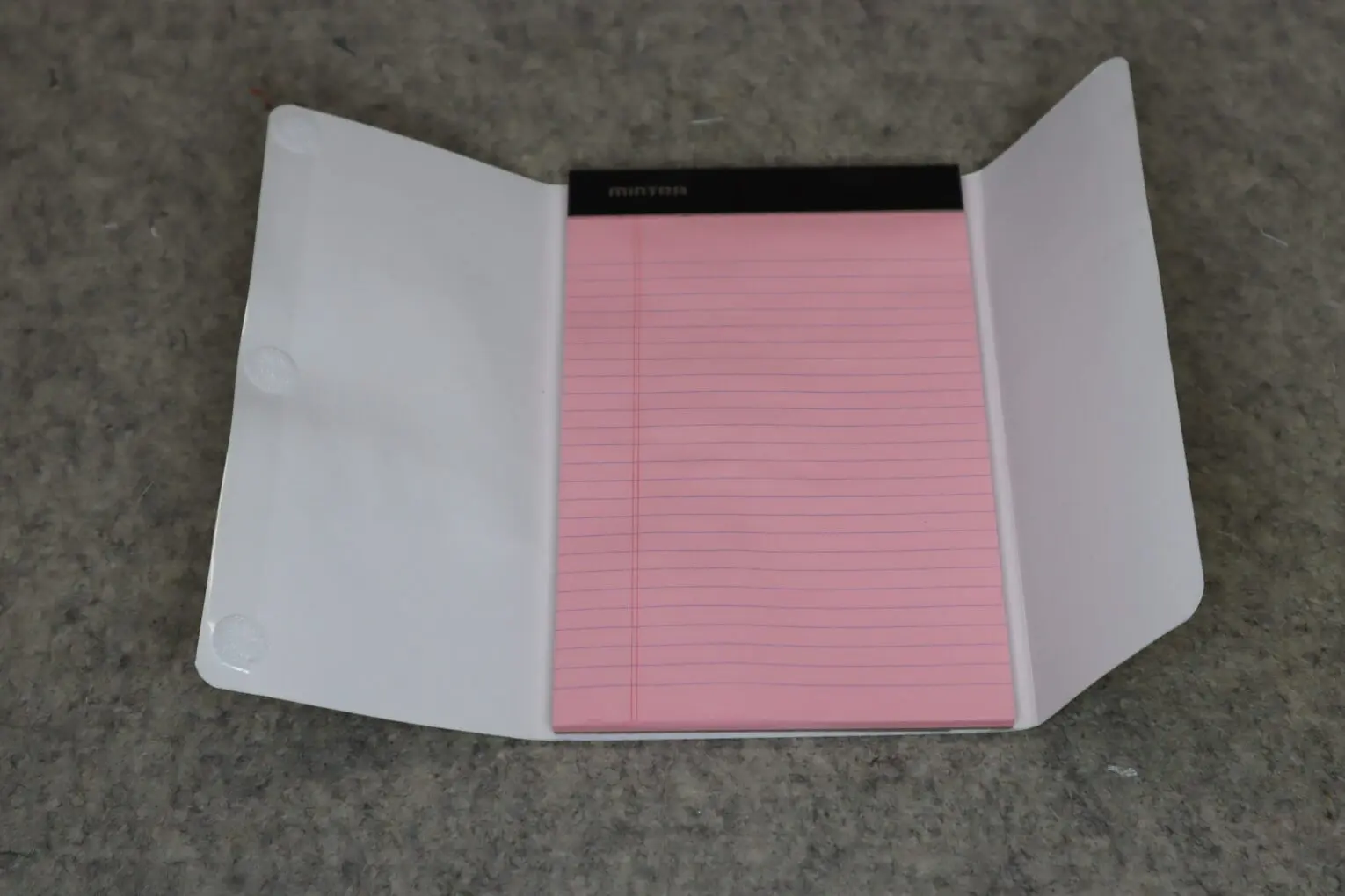 An open folder containing a pink lined notepad on a gray surface.