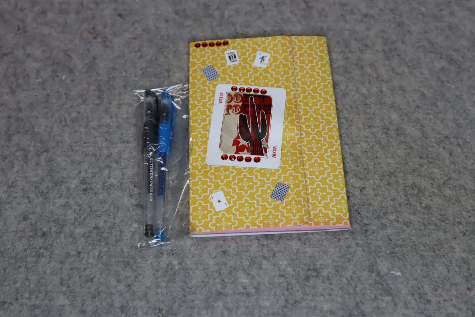 Yellow notebook with playing card designs and a pen on a grey surface.