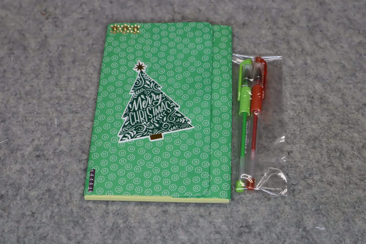 Green notebook with a Christmas tree sticker and a pen set in plastic.