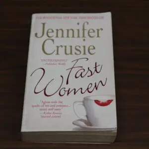 A paperback book titled 'Fast Women' by Jennifer Crusie on a wooden surface.