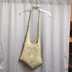Handmade knitted beige tote bag hanging on a hanger.