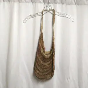 Brown woven shoulder bag hanging on a wire hanger against a white curtain.