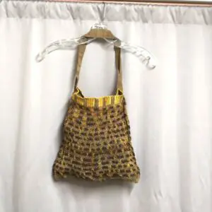 Handwoven bag with intricate patterns hanging on a white curtain.