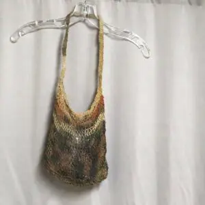 A fringed, multicolored knitted bag hanging on a clear hanger.
