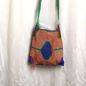 Colorful, handmade knitted bag with a shoulder strap against a white curtain.
