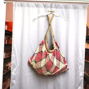 Colorful plaid handbag hanging on a wooden hanger against a white curtain.