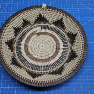 Handwoven circular basket with star designs on a blue grid background.