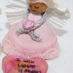 A small angel doll holding a pink heart with a 'True Love' message.