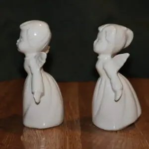 Two white ceramic figurines of girls in dresses facing each other.