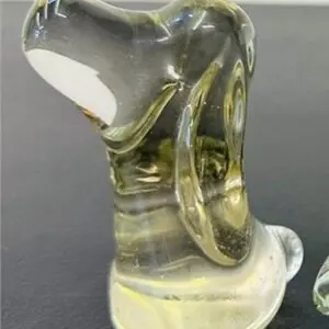 Clear glass sculpture with a yellow tint on a dark surface.