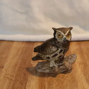A detailed owl sculpture perched on a wooden base on a hardwood floor.