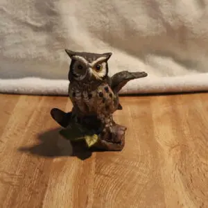 A small owl figurine perched on a branch on a wooden surface.