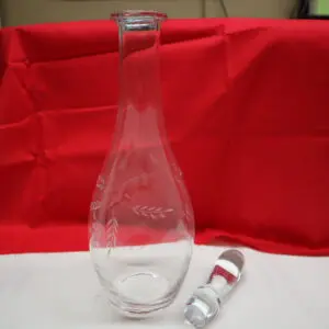 A clear glass bottle with a stopper, set against a red and white background.