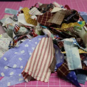 Pile of colorful fabric scraps on a pink cutting mat.