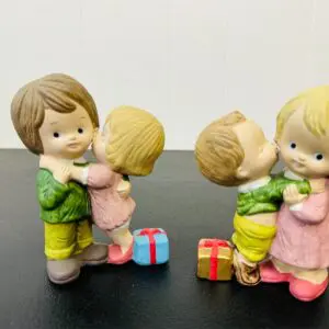 Two pairs of child figurines exchanging gifts with smiles.