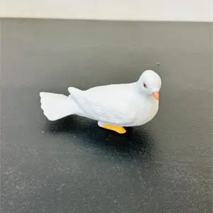 A small white bird figurine with orange feet on a dark surface.