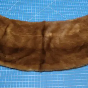 A brown fur collar laid out on a blue cutting mat.
