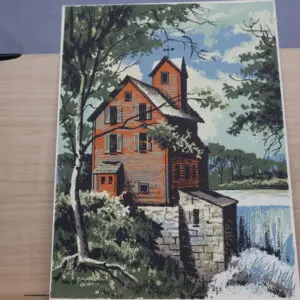 A rustic house by a river with surrounding trees under a blue sky.