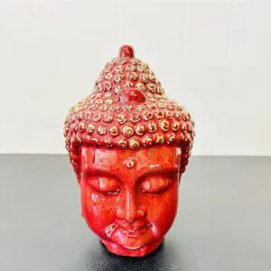 Red Buddha head sculpture adorned with small decorative beads.