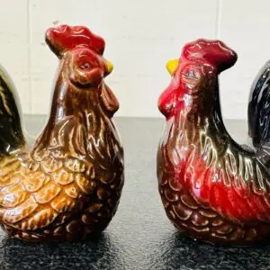 Two ceramic rooster figurines with detailed painting on a dark surface.