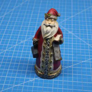 A small Santa Claus figurine with a lantern, standing on a blue grid surface.