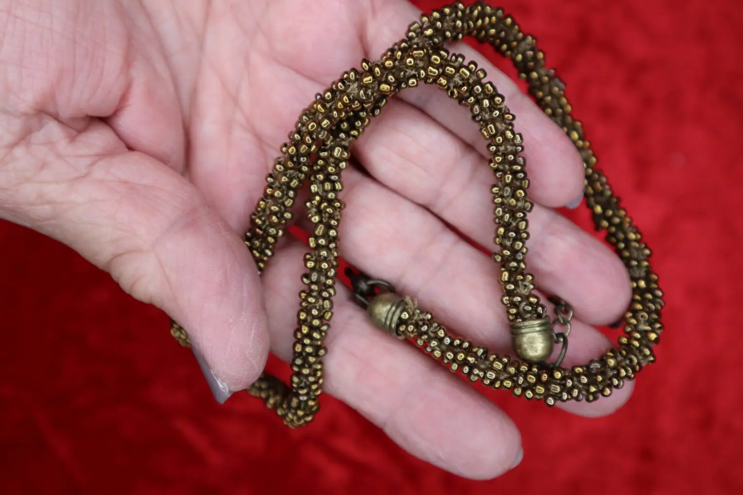 Bronze beaded necklace held in a hand.