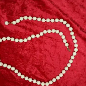 White beaded necklace displayed on red fabric.