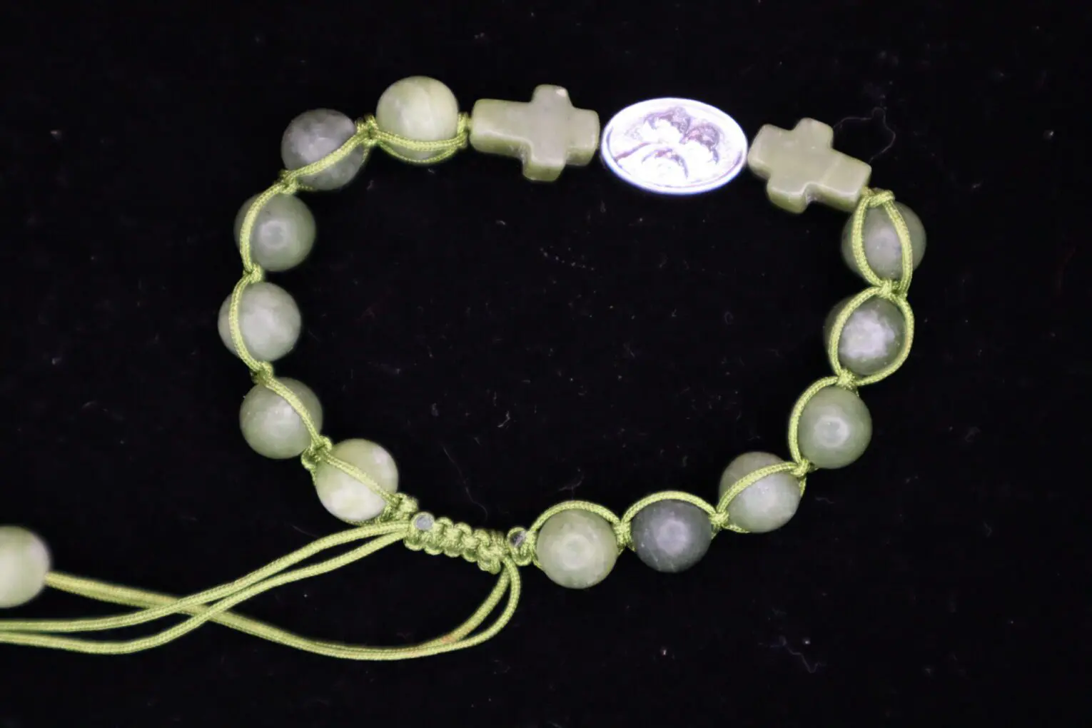 Green beaded bracelet with cross and oval charm.