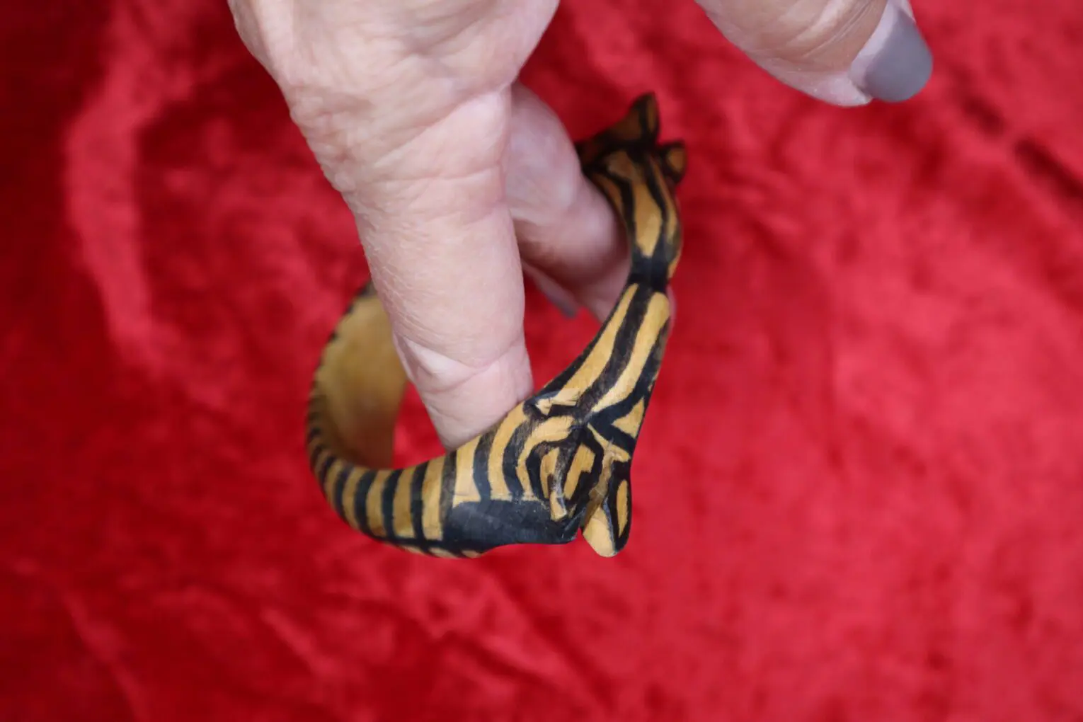 Hand holding a wooden bracelet with tiger design.