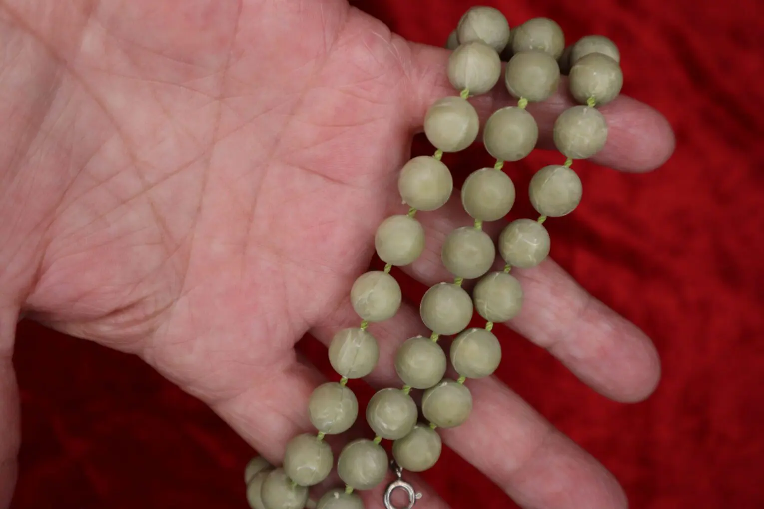 Green beaded necklace held in a hand.