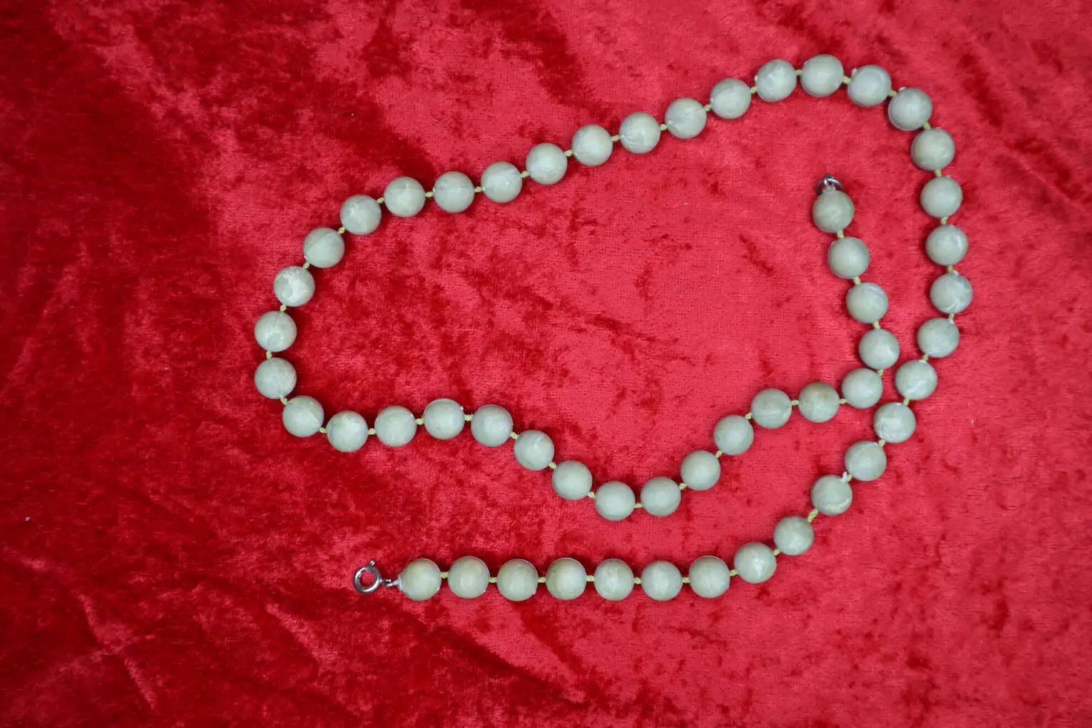 Light green beaded necklace on red background.