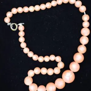 Peach-colored beaded necklace displayed on black background.