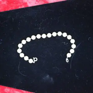 White beaded bracelet displayed on black fabric.