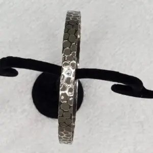 Textured silver bracelet displayed on a stand.