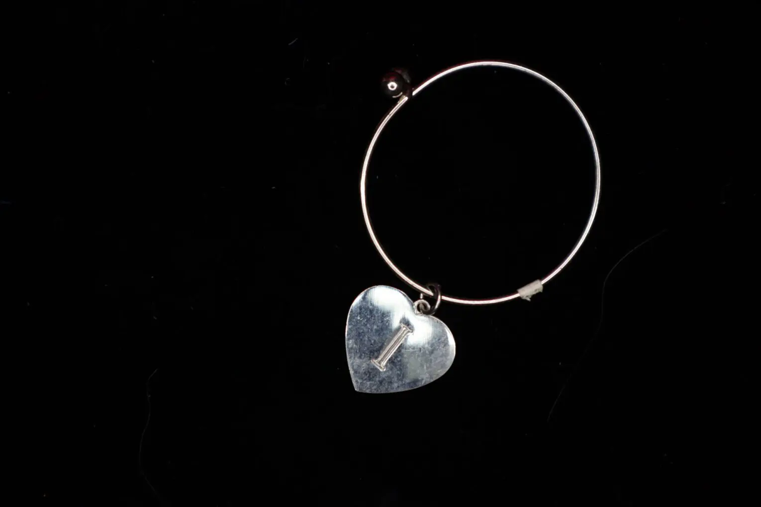 Silver hoop earring with heart-shaped pendant.