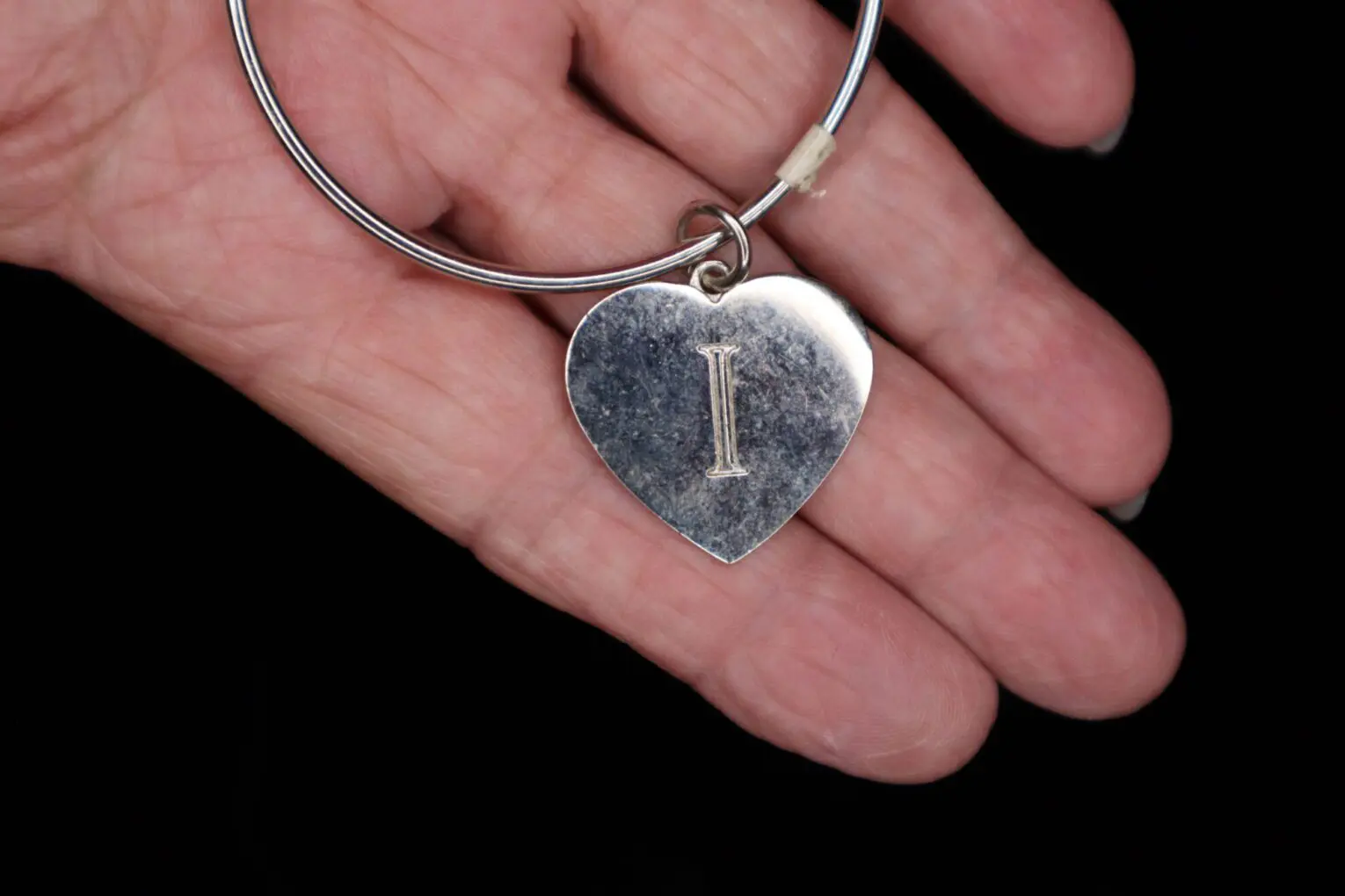 Silver heart-shaped pendant held in a hand.