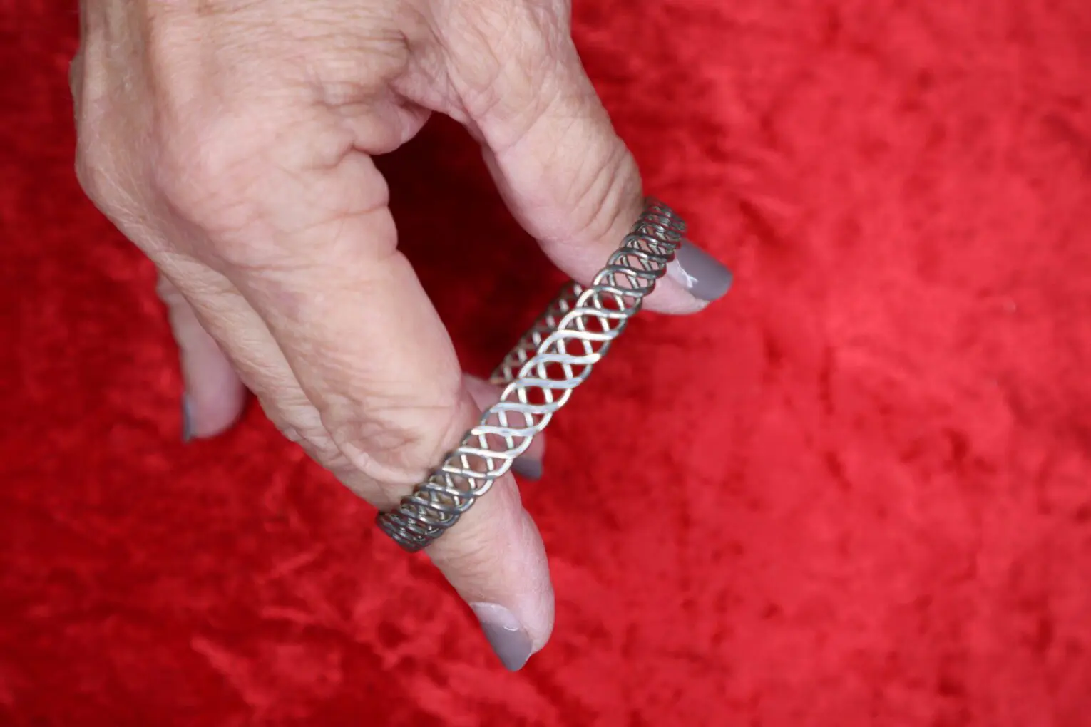 Intricate silver bracelet held on a red background.